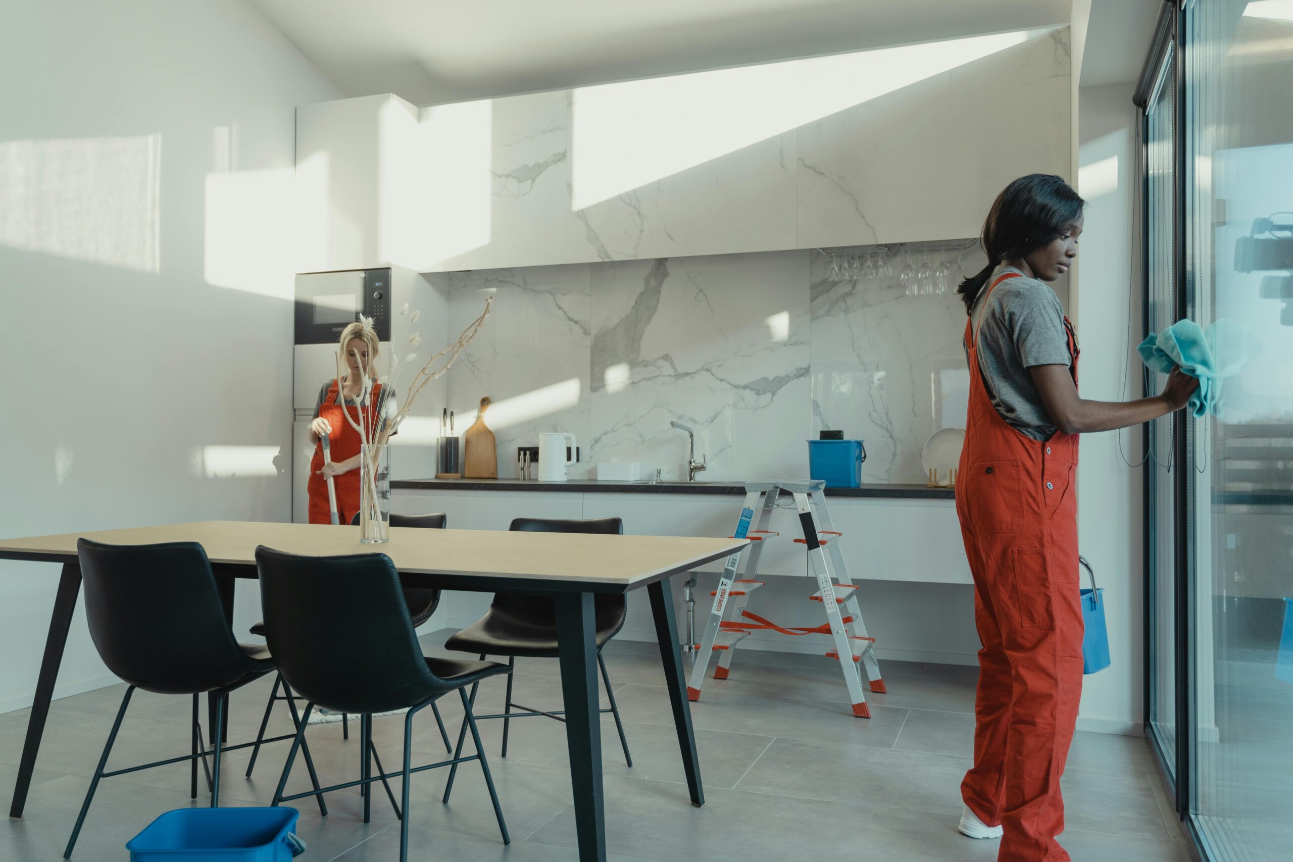 Two women in red overalls are standing by a table.